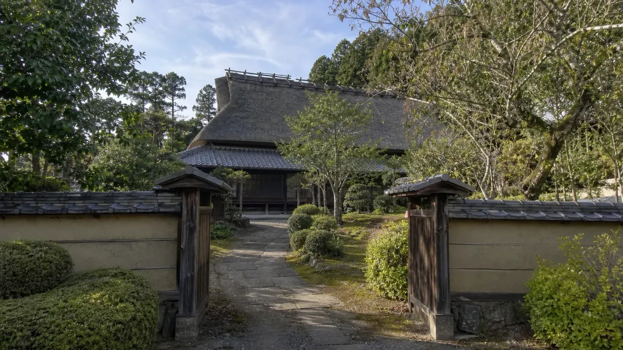 常総市の坂野家住宅を思わせる、薬医門の先に茅葺き屋根の古民家と庭が見える里山の風景