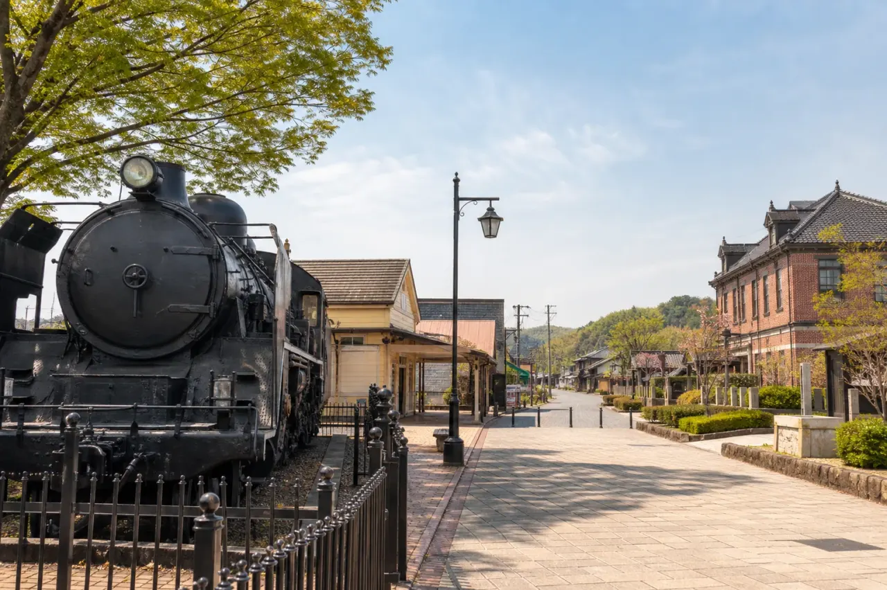 黒い蒸気機関車と駅前の落ち着いた街並みを描いた、栃木の鉄道散歩イメージ