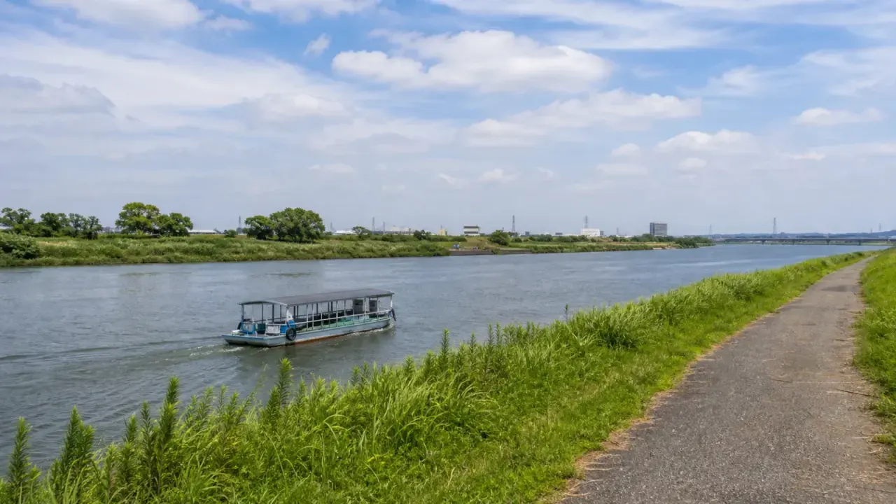 取手市の利根川で、小堀の渡しの小さな船が水面を進み、河川敷と青空が広がるイメージ