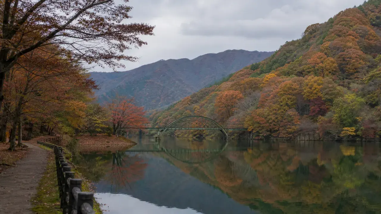 安中市の碓氷湖を思わせる紅葉の山、水面に映る色、湖畔の小さな橋と遊歩道